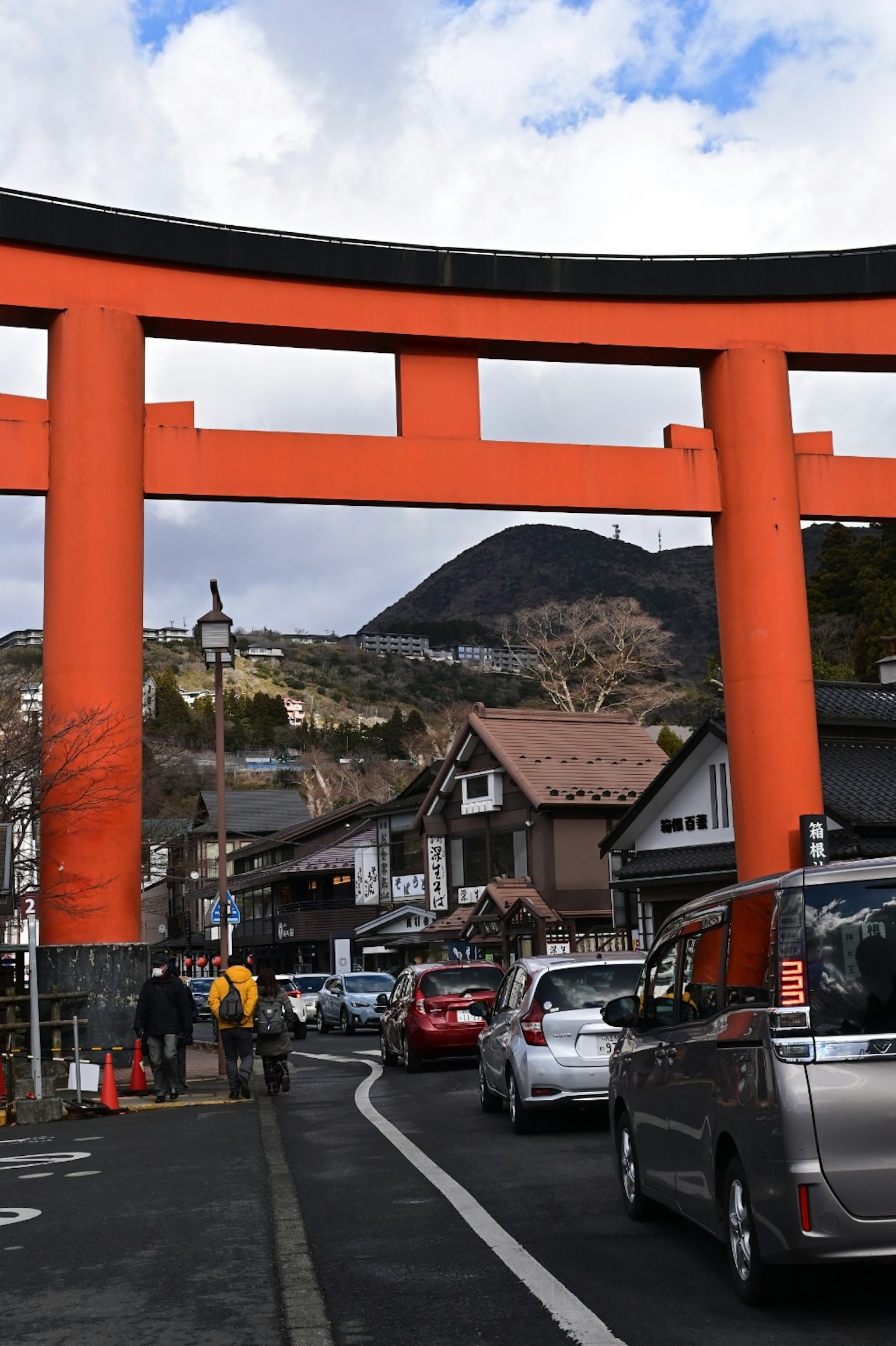 Gerbang torii oranye besar dengan latar belakang gunung dalam pemandangan jalan