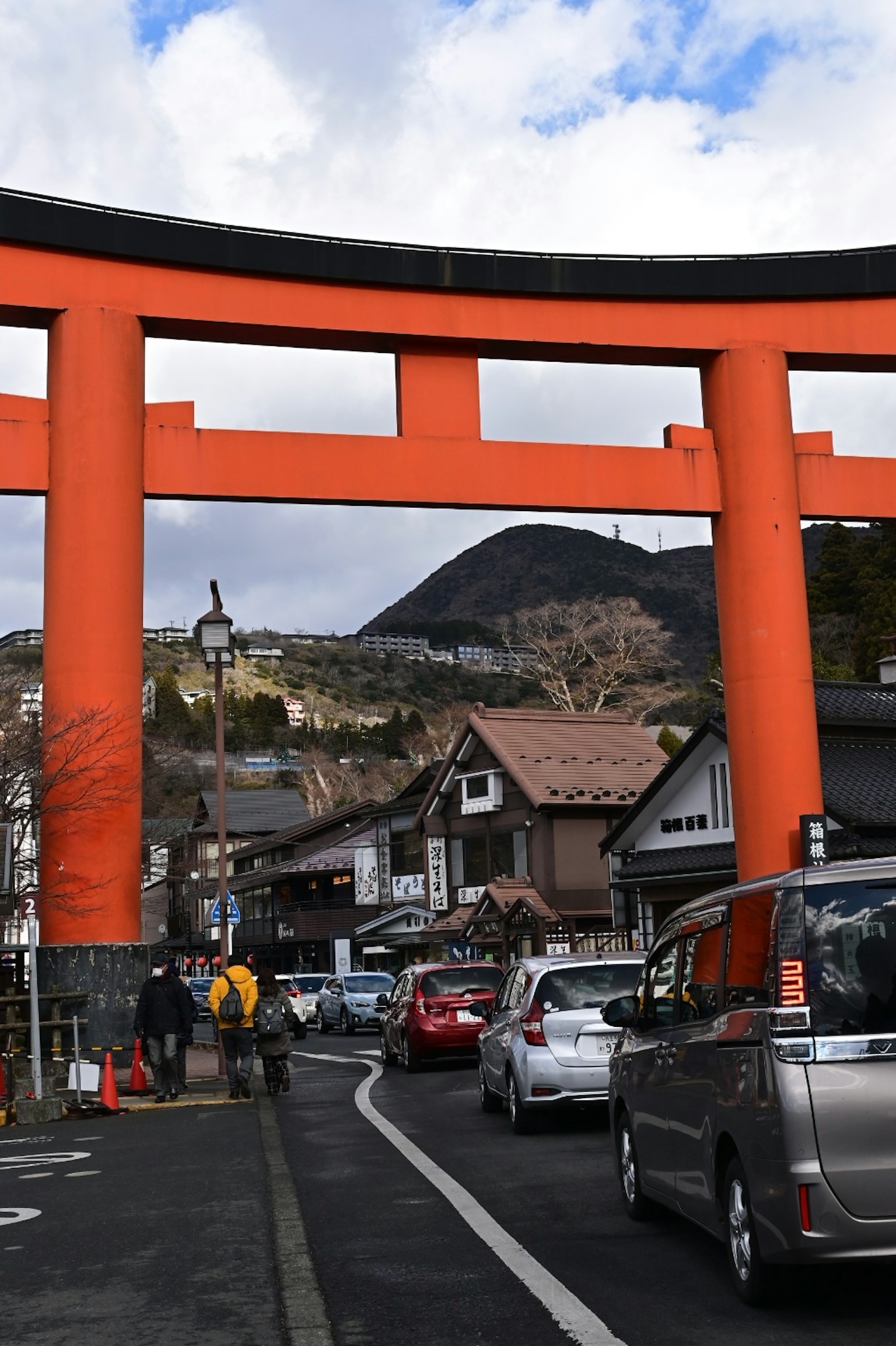 Large orange torii gate with a mountain backdrop in a street scene