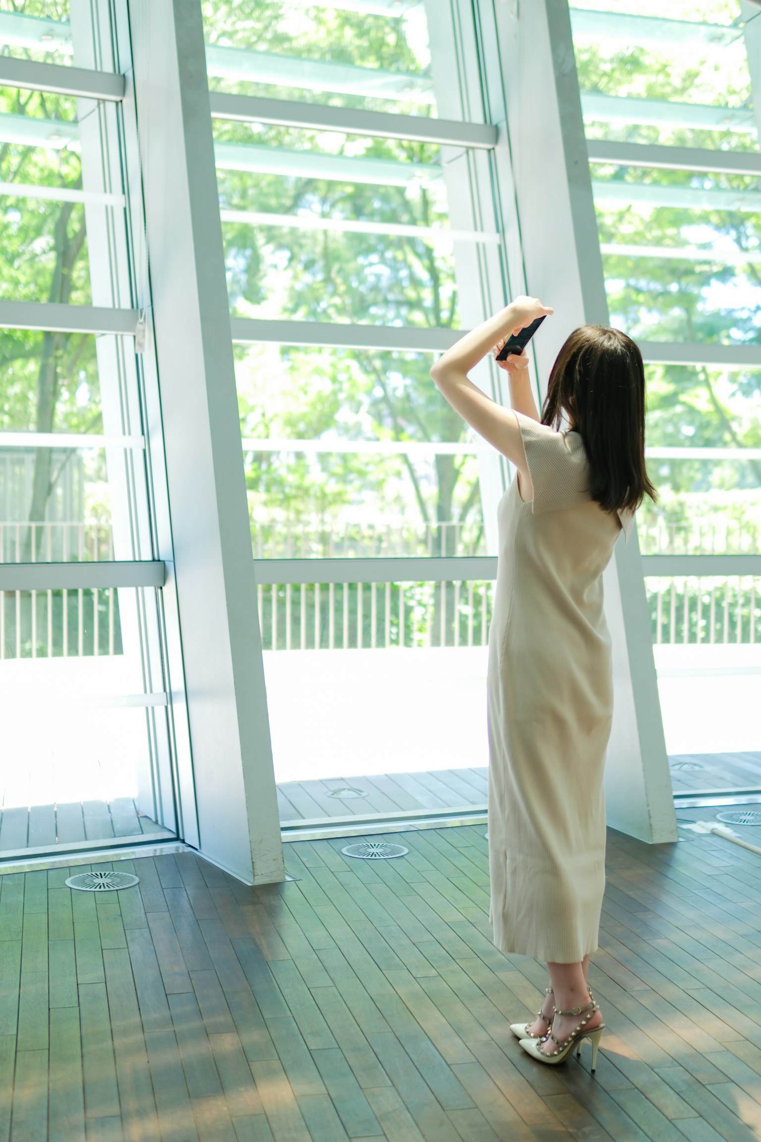 Una mujer de pie junto a la ventana tomando fotos Lleva un vestido blanco y se puede ver un paisaje verde brillante afuera