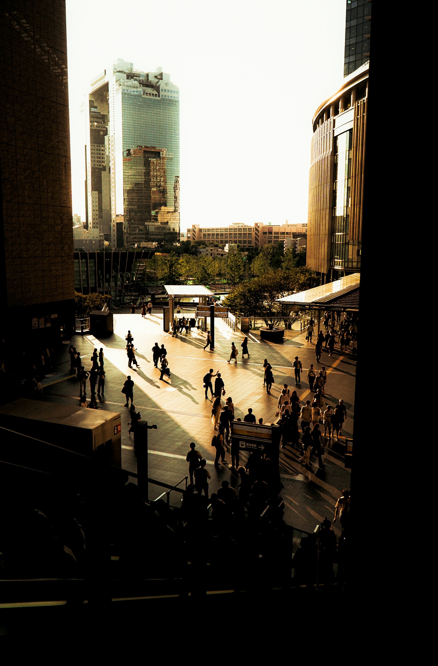 Personas caminando en una plaza de la ciudad durante el atardecer con edificios modernos