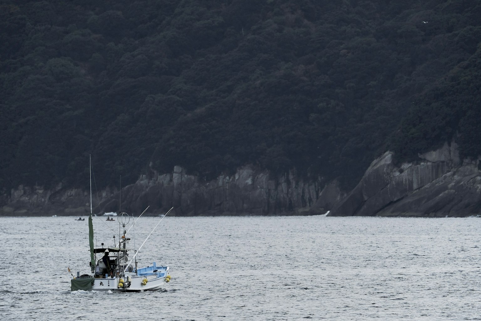 Ein kleines Fischerboot, das in ruhigen Gewässern mit Bergen im Hintergrund fährt