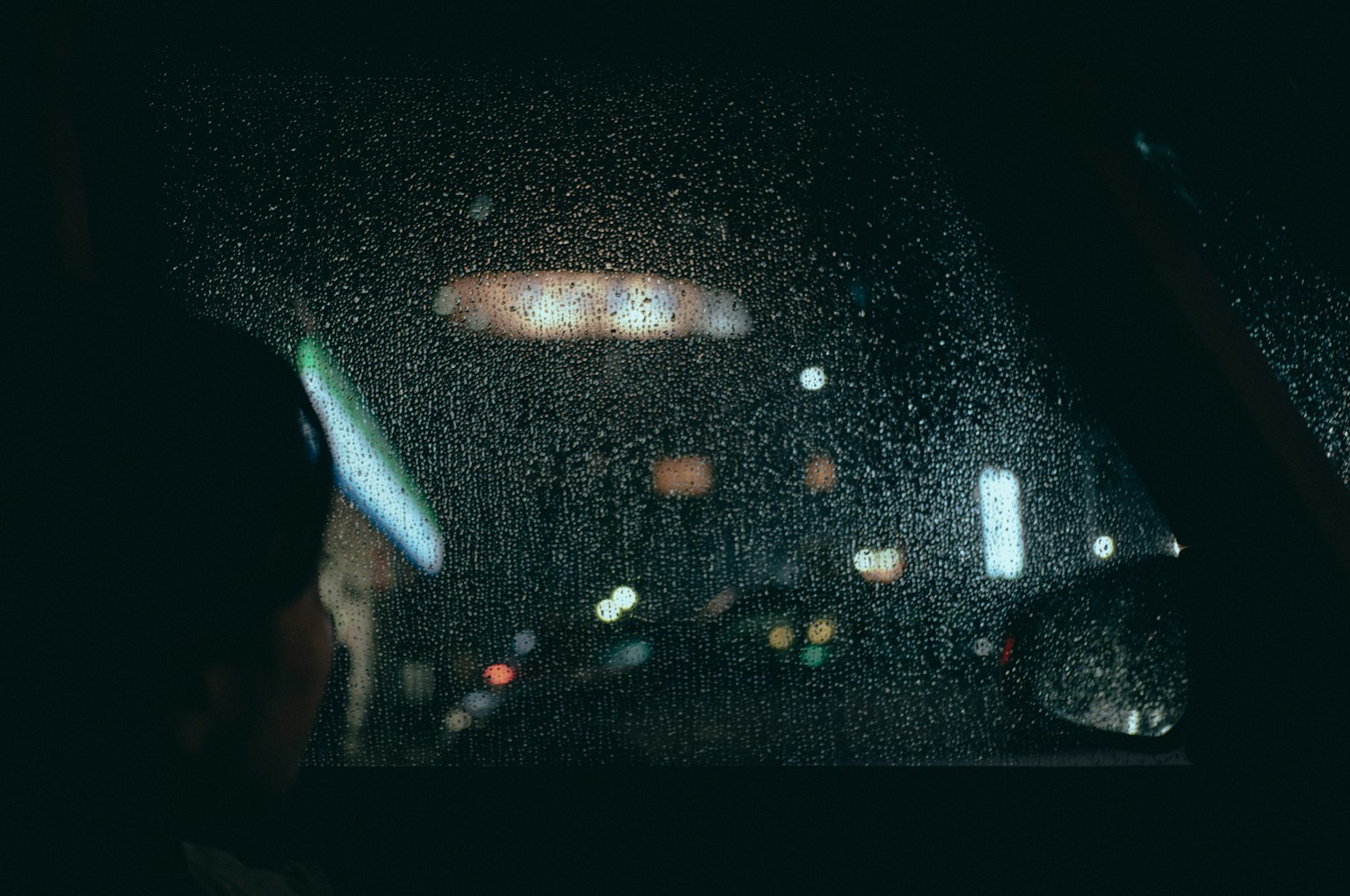 Night cityscape viewed through a rain-soaked window with a child's profile