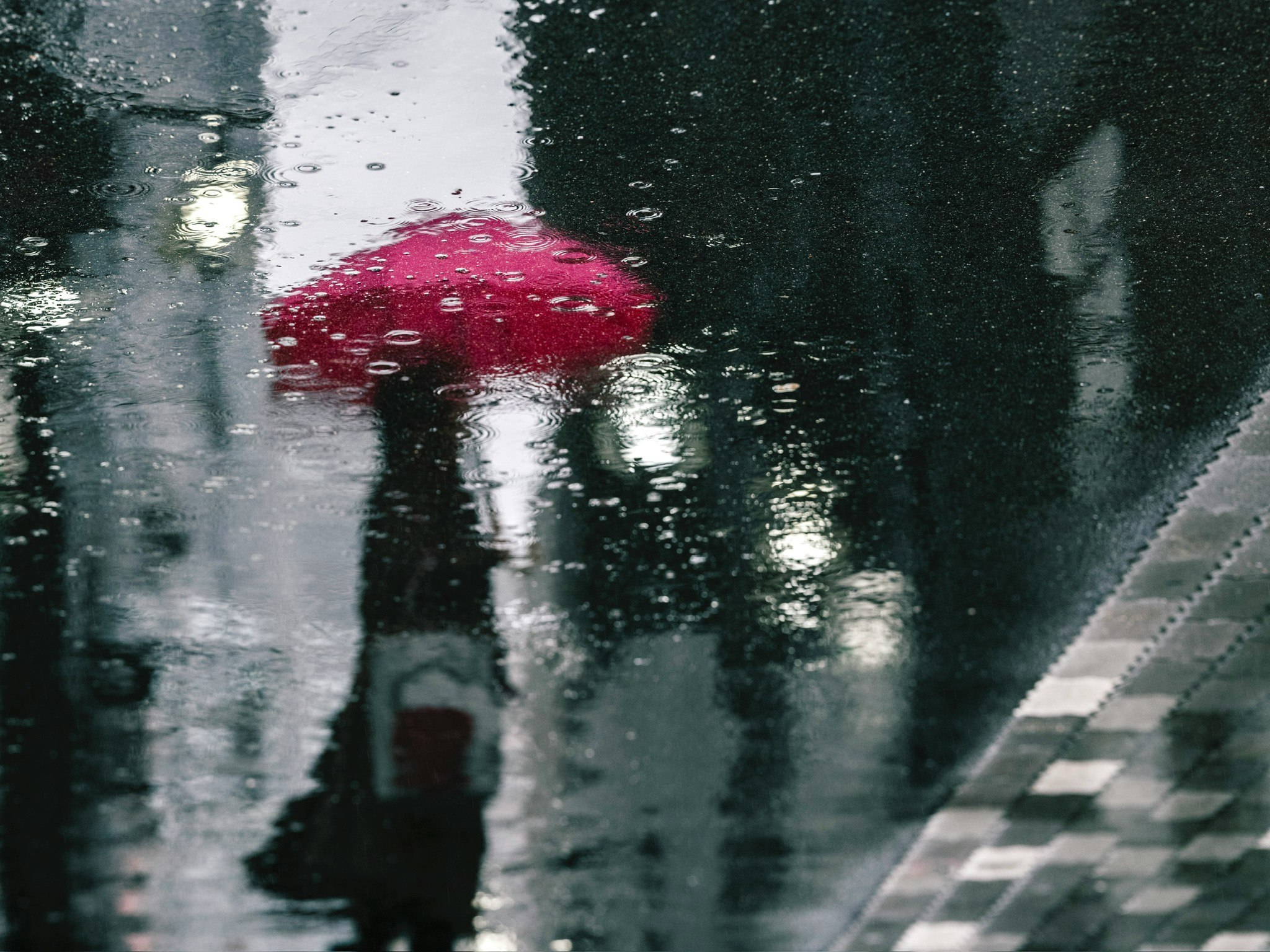 Straßenecke mit Regenschirmen und Silhouetten im Spiegelbild auf nassem Pflaster