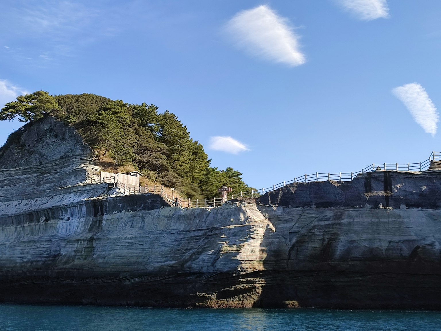 Scenica scogliera rocciosa con alberi verdi su sfondo di mare blu