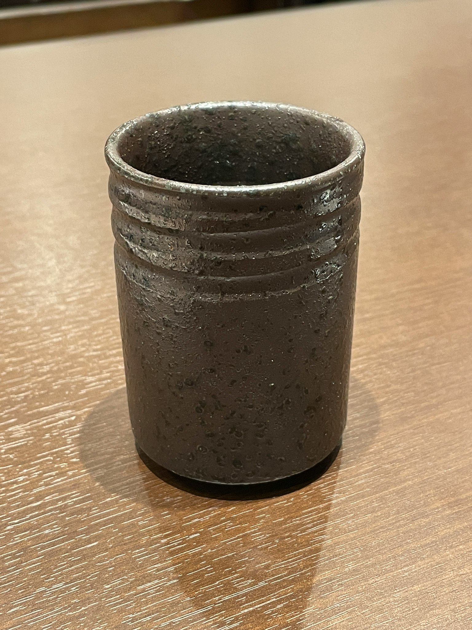 Eine dunkle Keramiktasse steht auf einem Holztisch