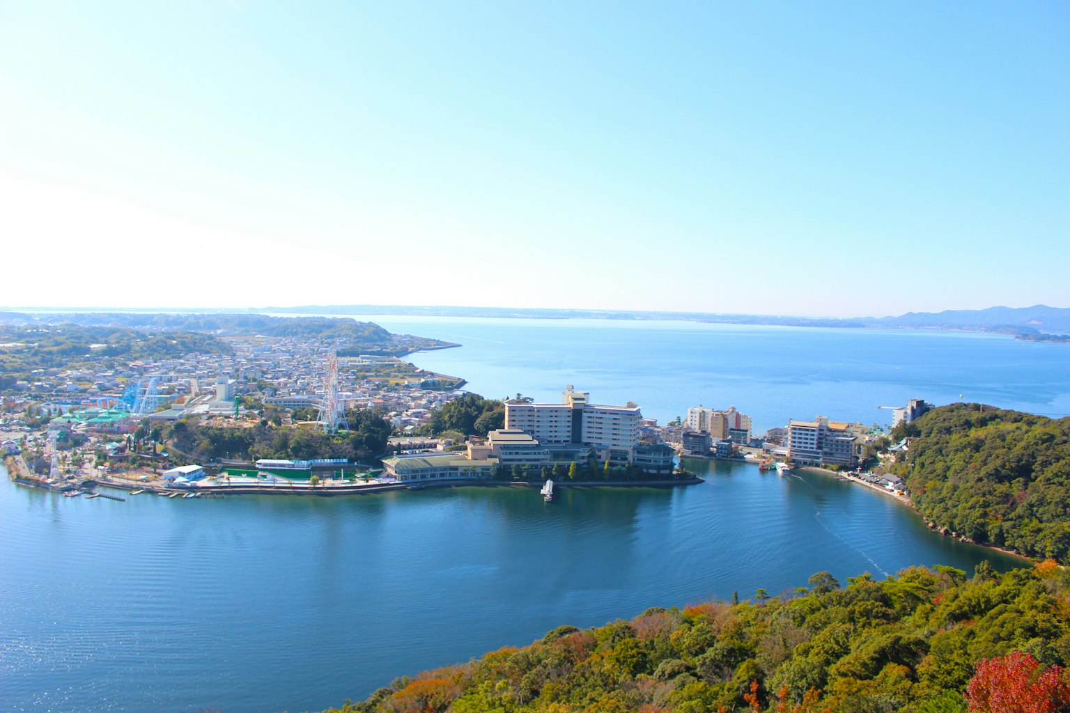 Vista panoramica di una città costiera circondata da montagne e mare blu chiaro