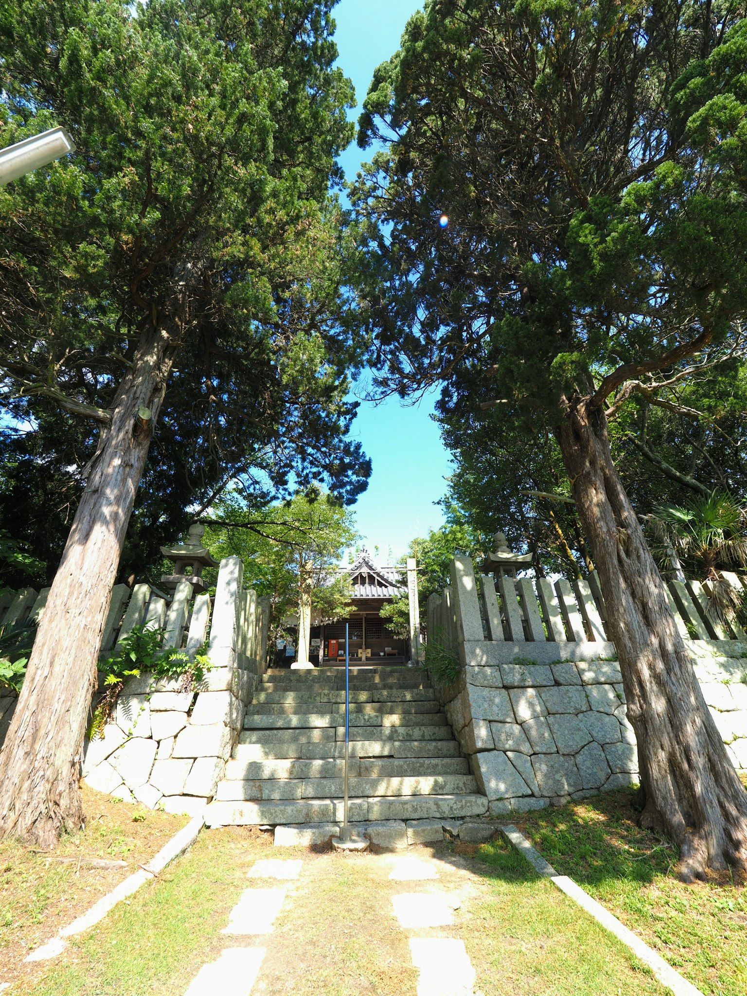 Entrée d'un sanctuaire entourée d'arbres hauts et d'escaliers en pierre