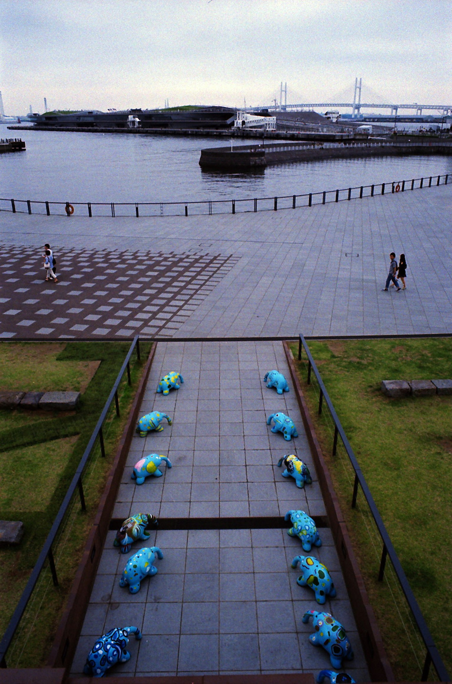 Blue frog sculptures arranged along a walkway in a park with a waterfront view