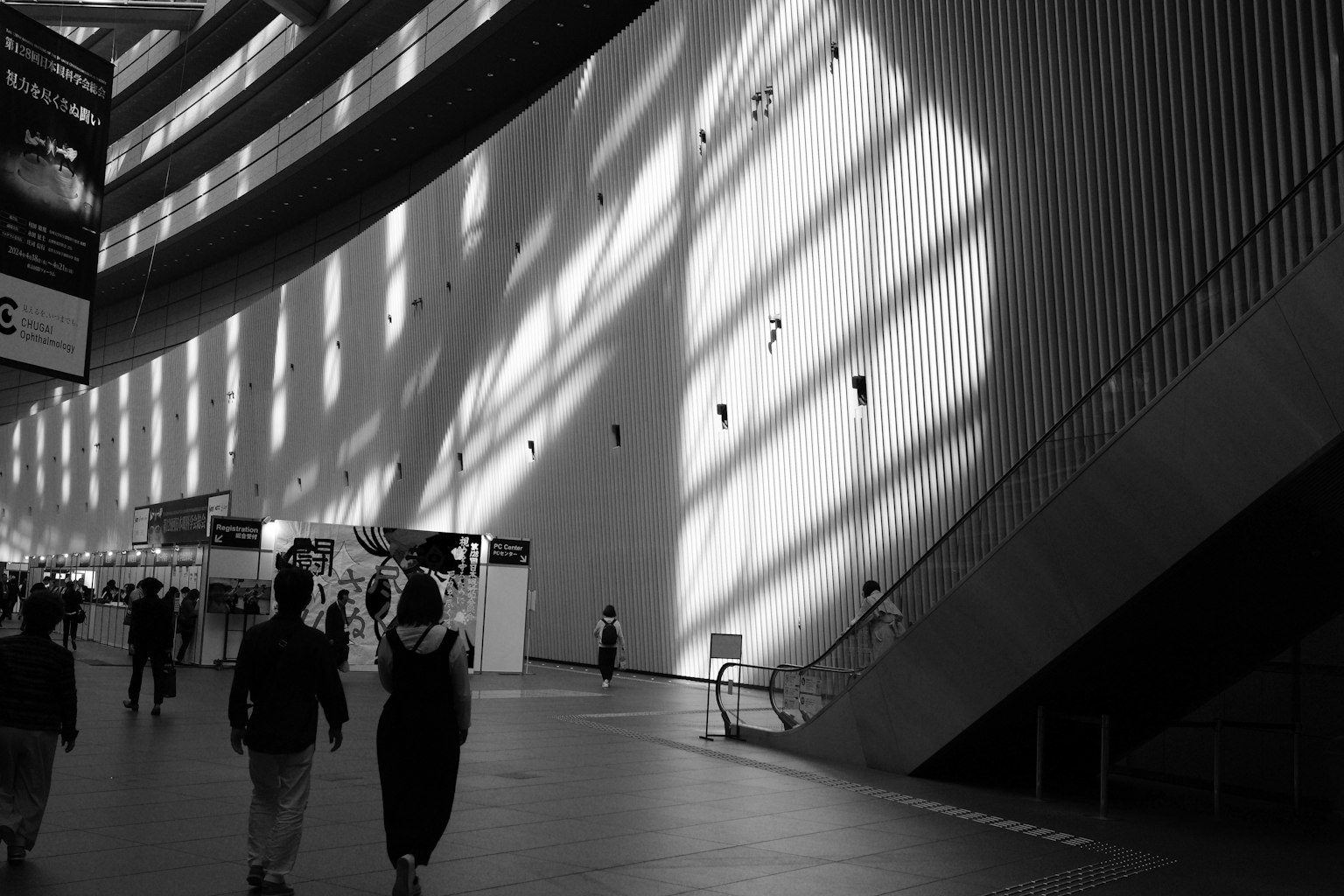 Black and white interior of a building with shadows on the wall and people walking