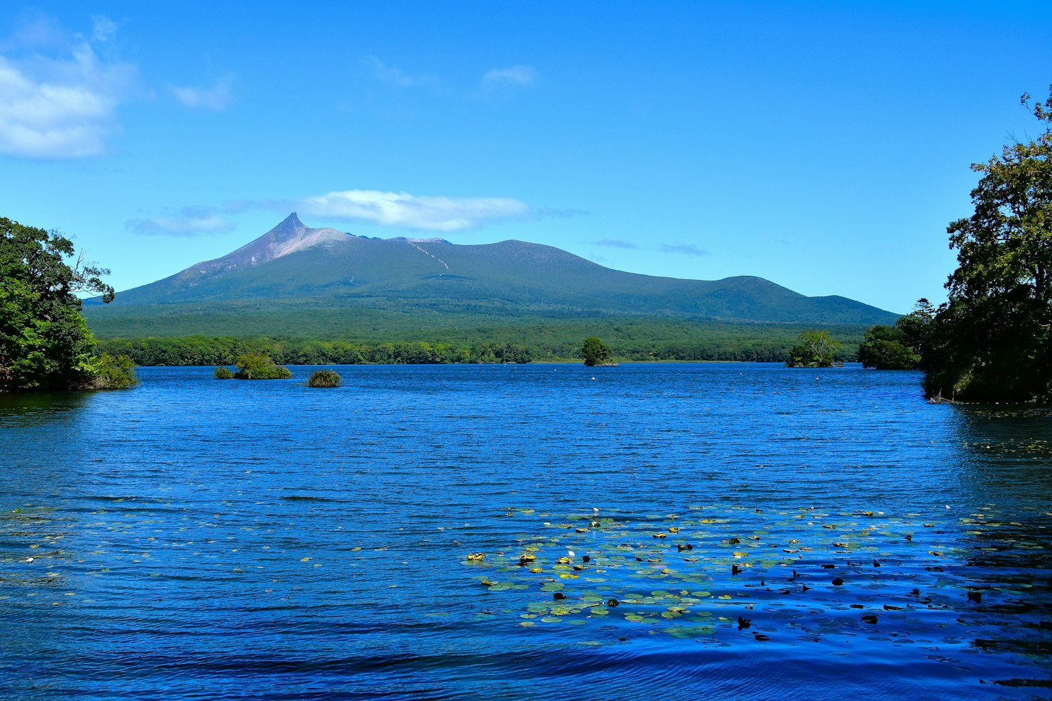 Un lago blu pittoresco con alberi verdi e un vulcano imponente sullo sfondo