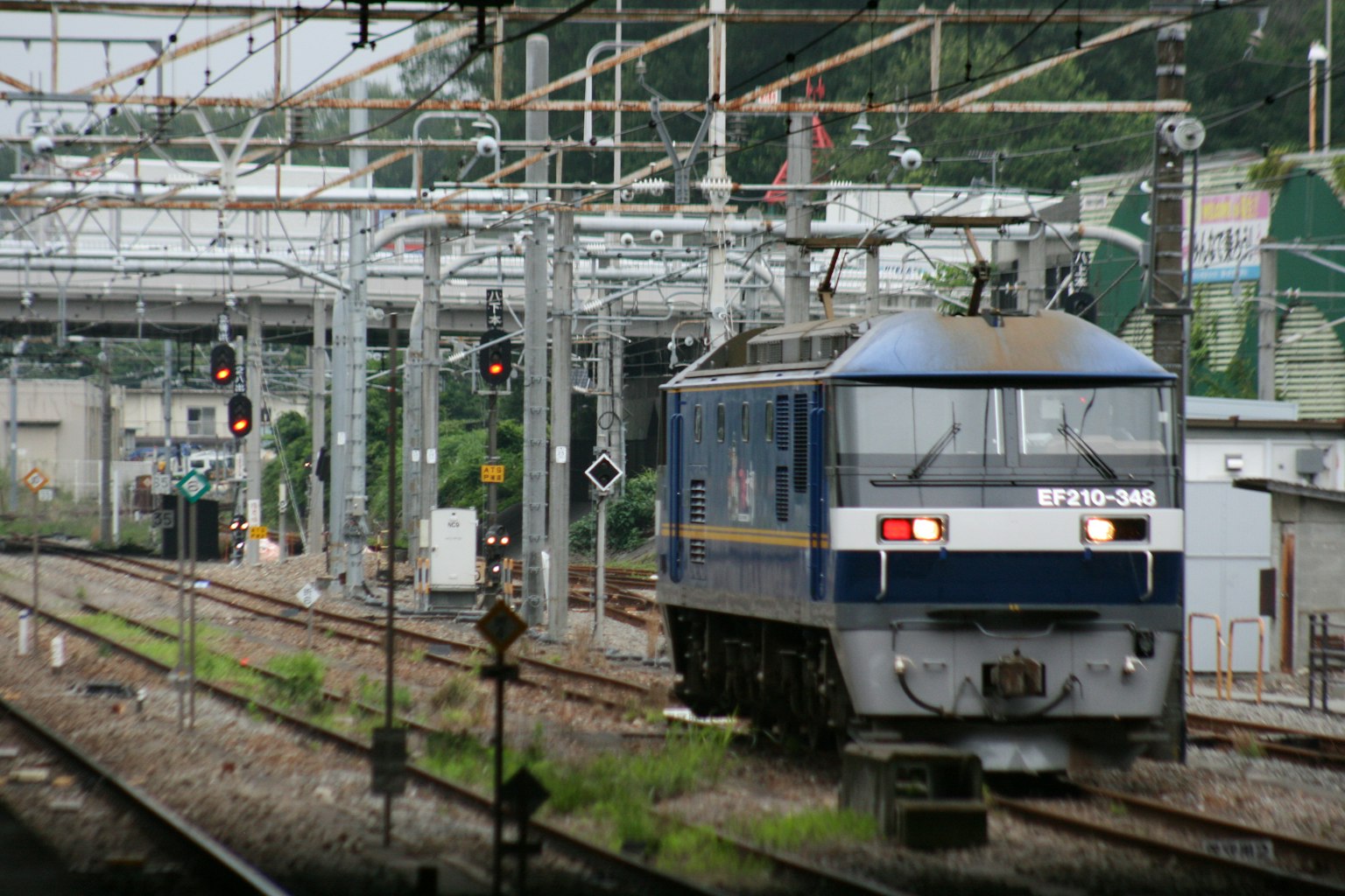 Kereta biru bergerak di rel dengan sinyal kereta api di latar belakang
