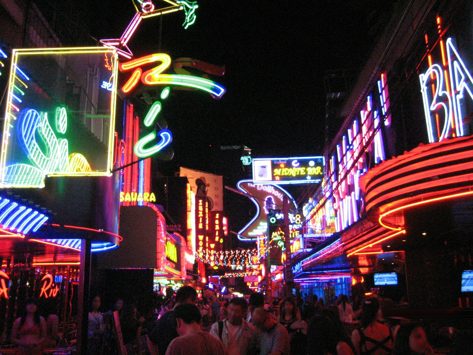 Pemandangan kehidupan malam yang bersemangat dengan papan iklan neon berwarna-warni dan kerumunan