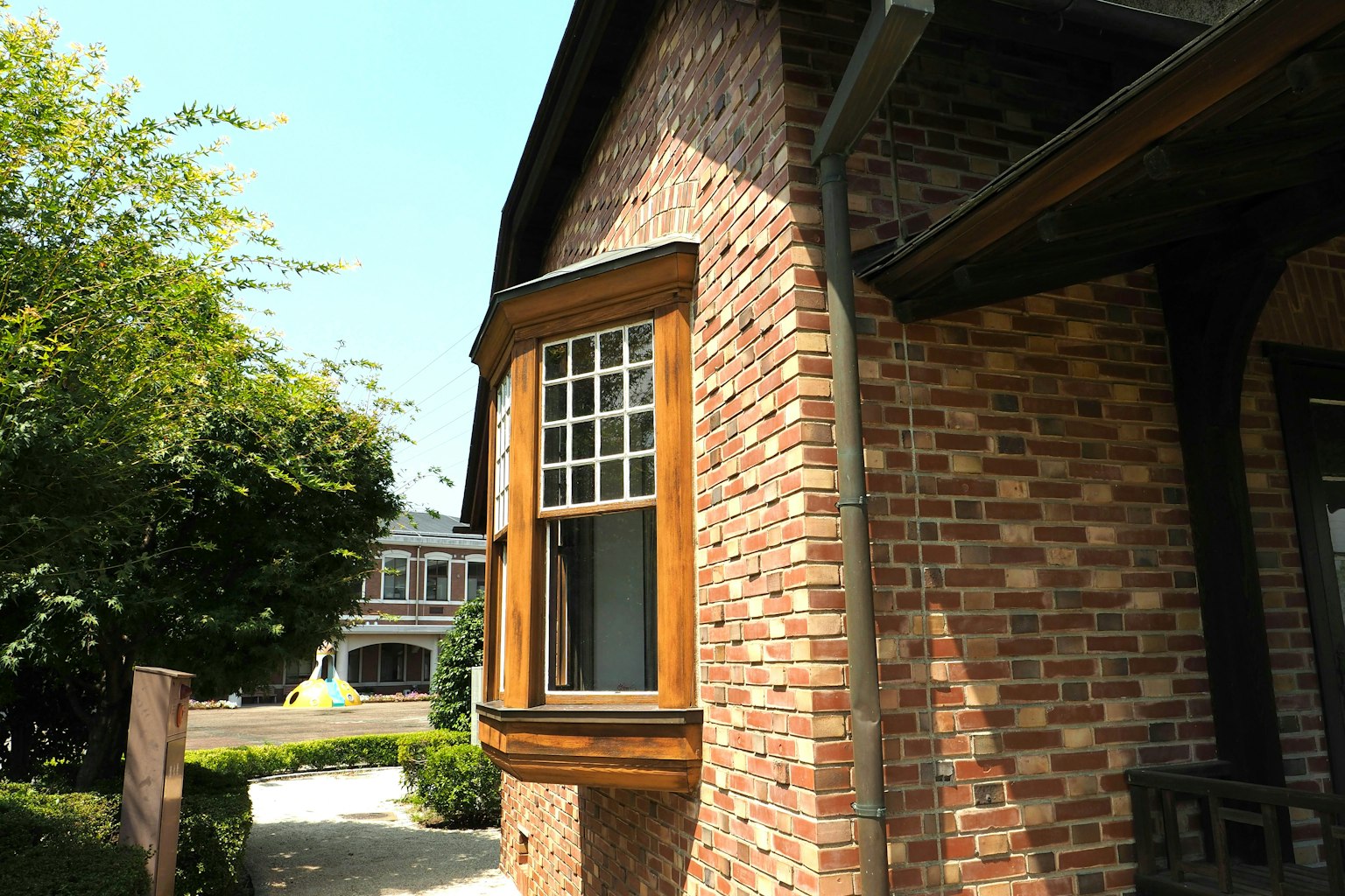 Corner view of a brick house featuring a wooden window and lush greenery