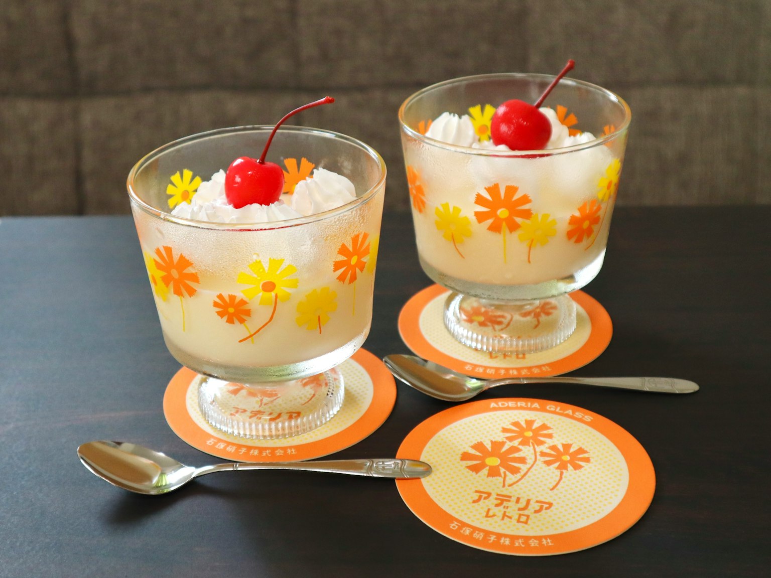 Two dessert cups topped with red cherries on a floral-patterned table