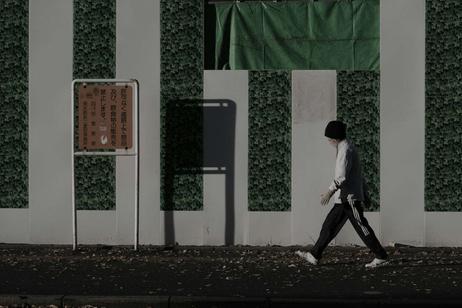 A person walking in front of a green wall with a sign in an urban setting