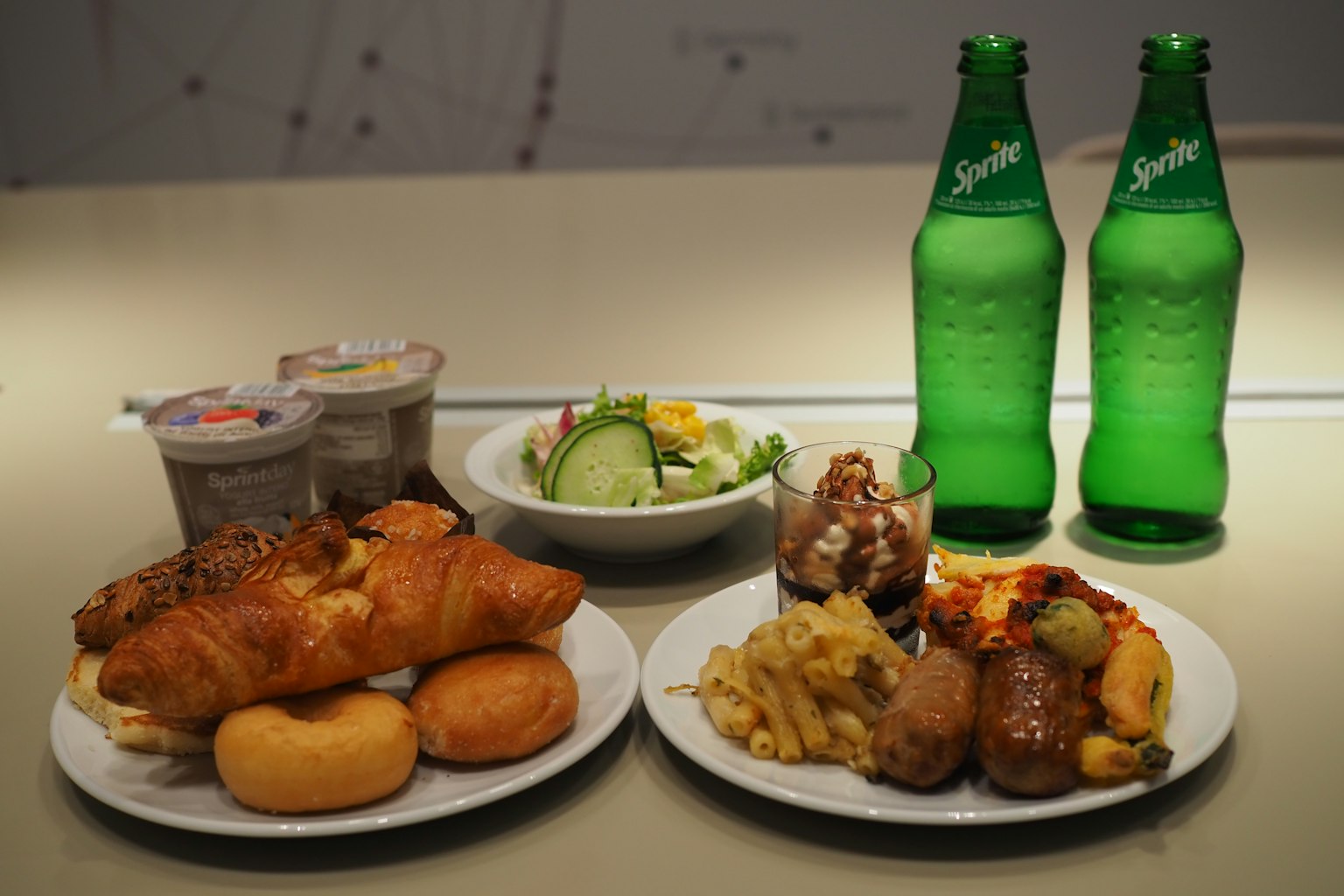 Một bữa ăn có bánh croissant, salad, món ăn kèm và đồ uống màu xanh