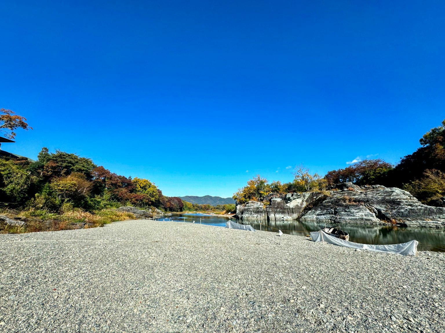 Paisaje de río sereno con cielo azul expansivo y camino de grava rocosa