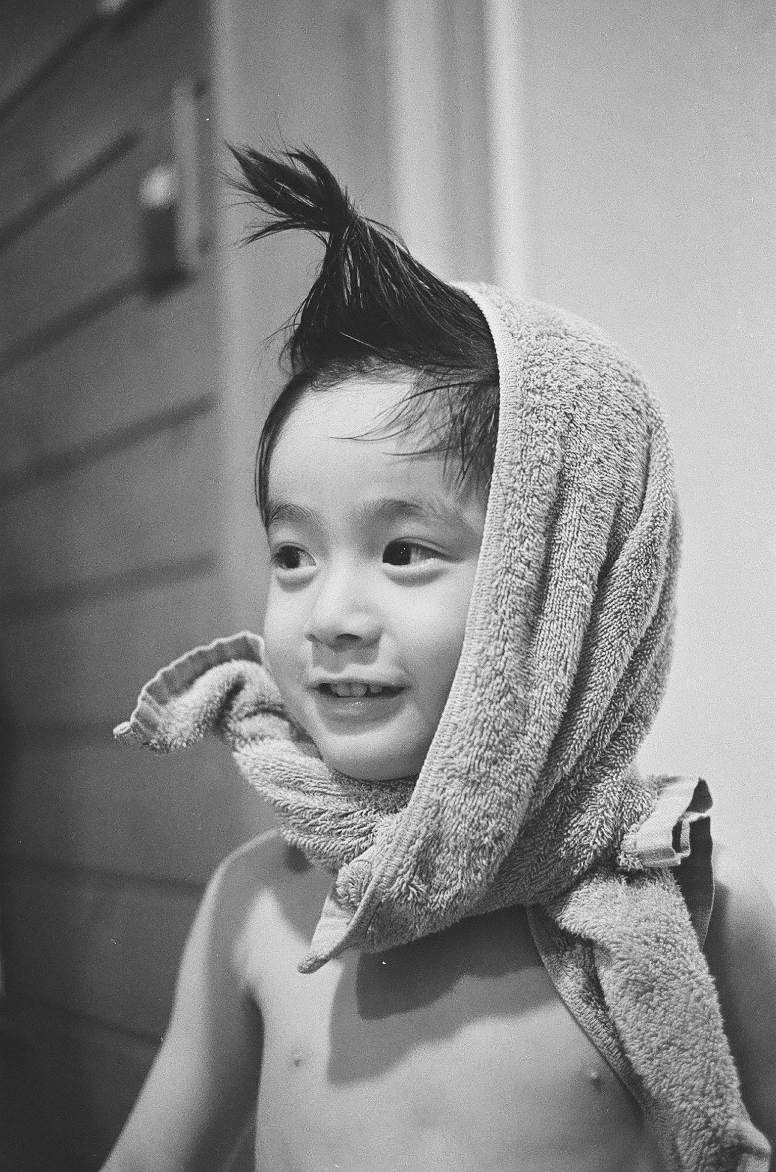 Un enfant souriant posant avec une serviette sur la tête dans une photo en noir et blanc