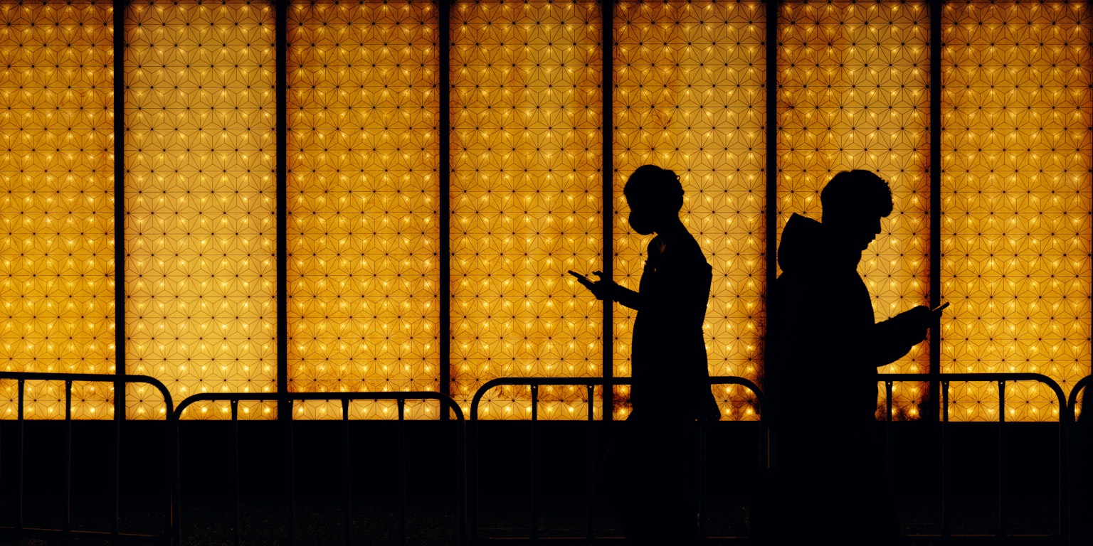 Silhouettes of people using smartphones against a backdrop of golden light at dusk