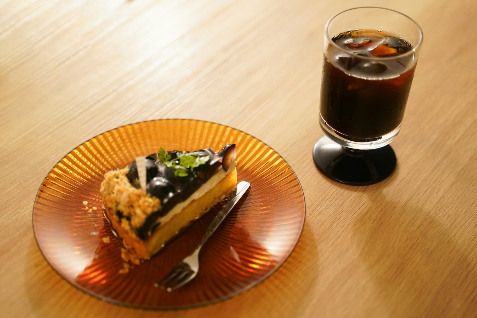 A beautiful photo of a cake and a drink The cake has chocolate and fruit toppings The drink is iced coffee in a glass