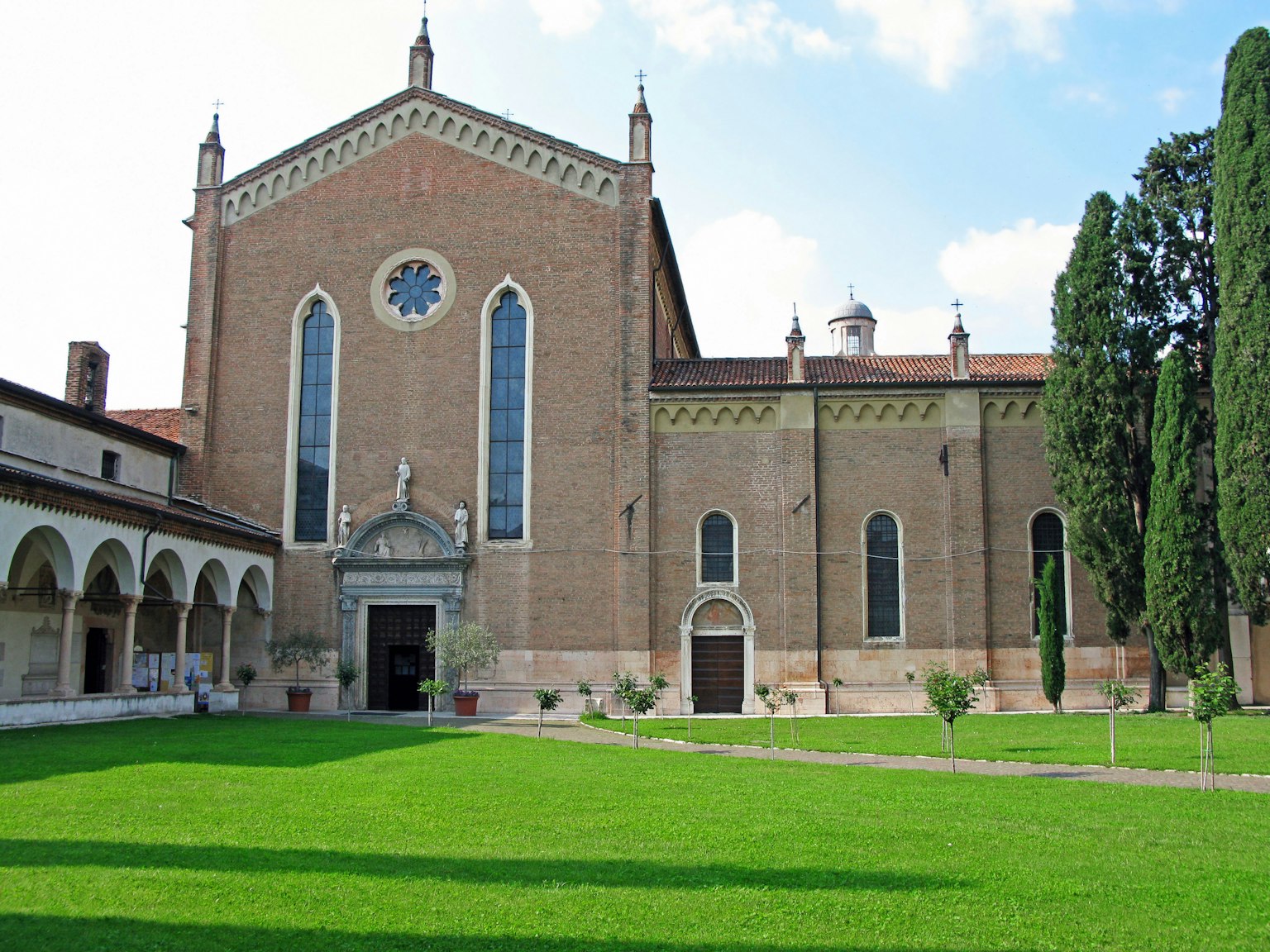 Esterno di una chiesa storica circondata da un prato verde lussureggiante con colonnato vicino e alberi alti