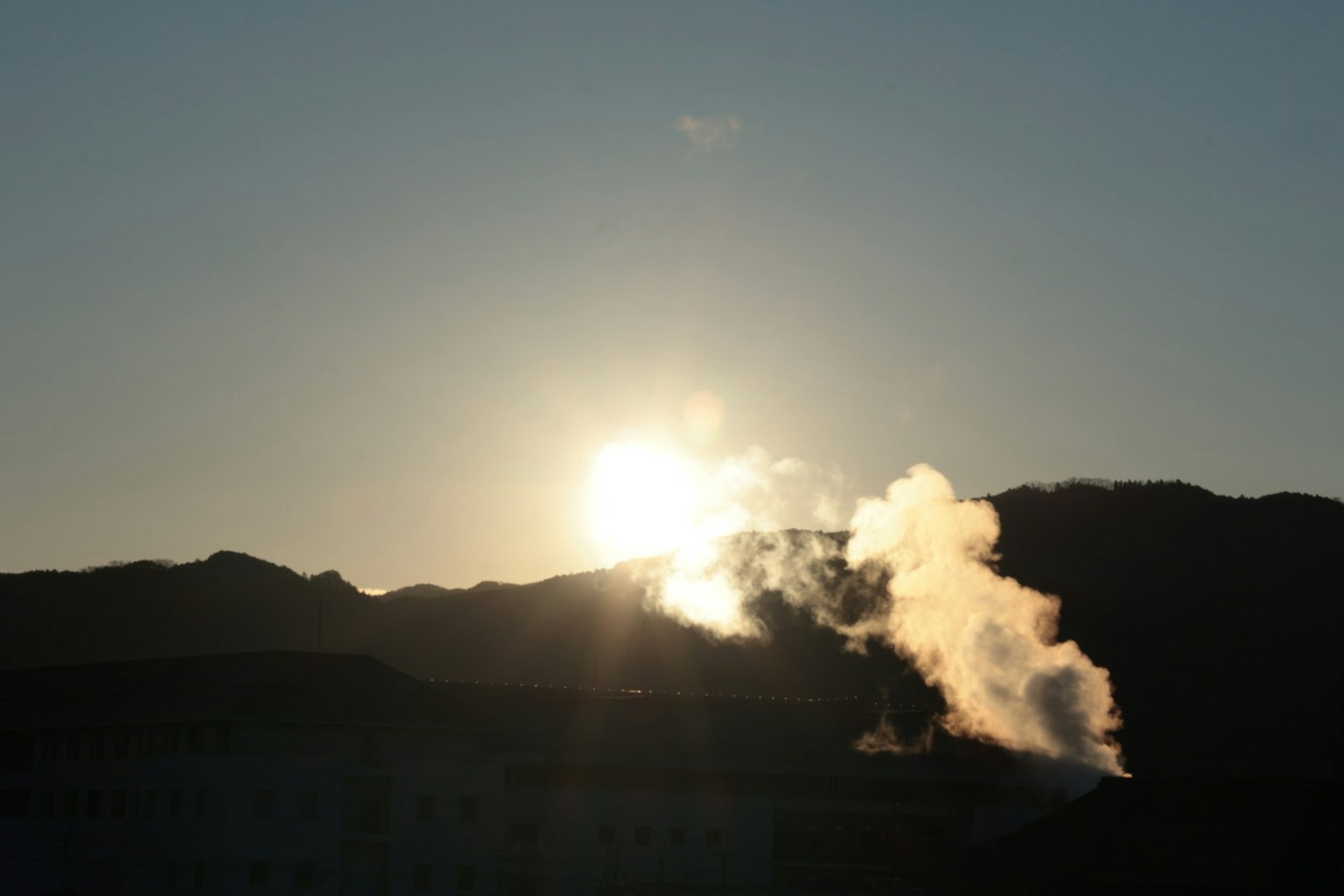 Tramonto dietro le montagne con fumi che si alzano in primo piano