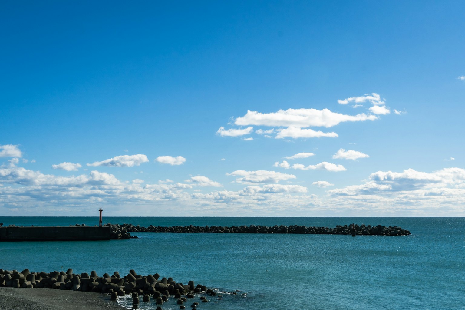Vue côtière avec un brise-lames sous un ciel bleu avec des nuages