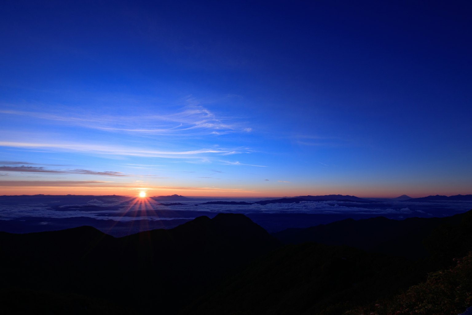 Schöne Landschaft mit der Sonne, die zwischen Bergen unter einem blauen Himmel aufgeht