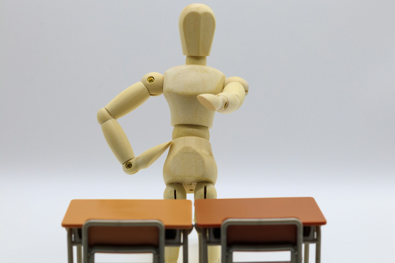 Maniquí de madera de pie frente a dos mesas señalando con una mano
