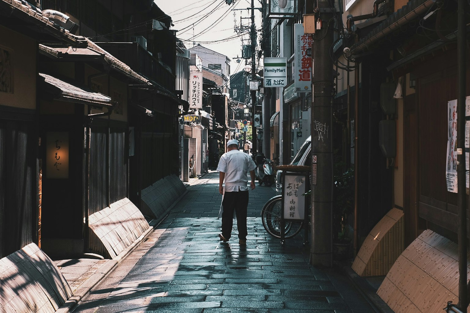 A person walking down a narrow alley with traditional buildings and overhead wires