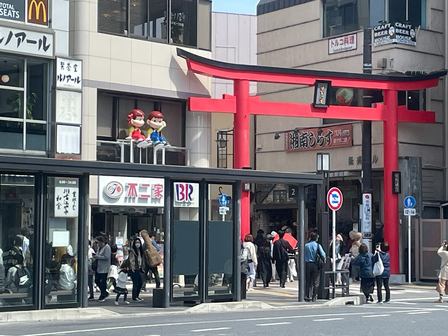 Una escena callejera vibrante con una puerta torii roja y numerosas personas caminando en una zona comercial concurrida