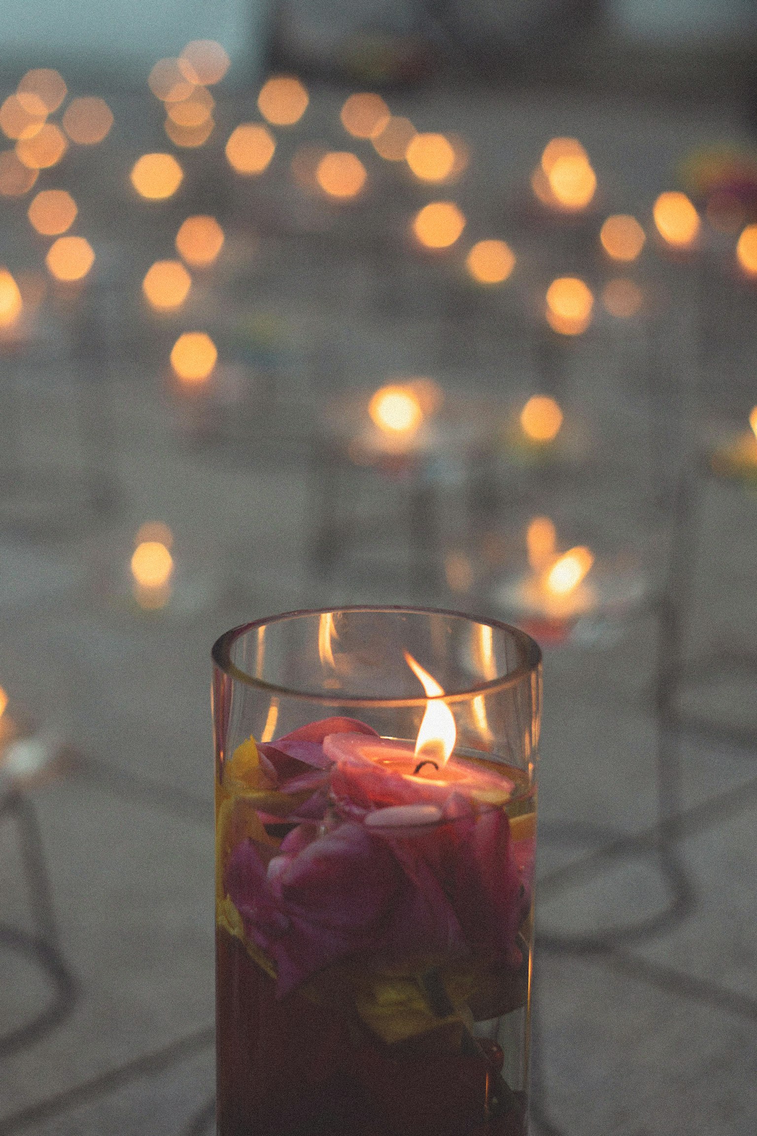 Primo piano di una candela in vetro con petali circondata da luci soffuse sullo sfondo