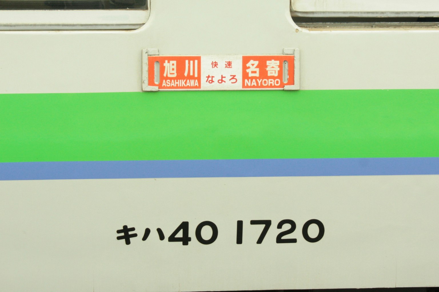 Sisi kereta Jepang dengan garis hijau dan biru serta nomor identifikasi dan nama stasiun
