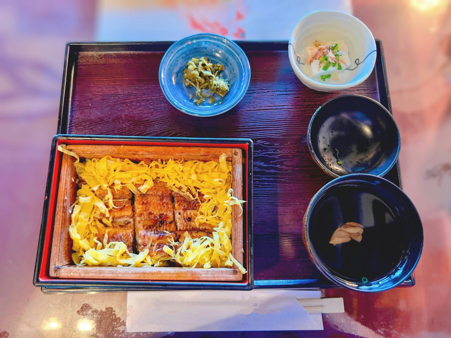 Conjunto de cocina japonesa presentado en una bandeja de madera con anguila a la parrilla y arroz acompañado de pequeños platos y sopa miso