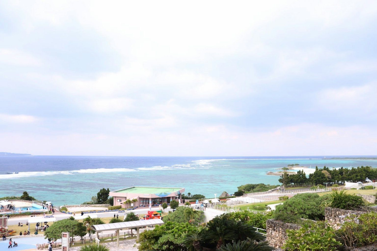 A scenic view of blue ocean and cloudy sky with green land and buildings