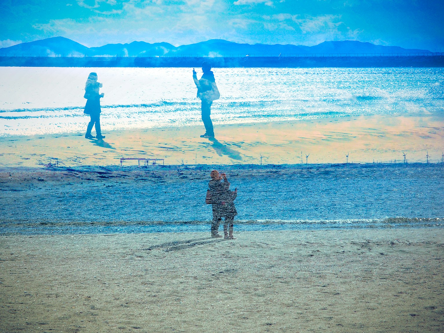 A scenic view of two people standing on the beach under a blue sky