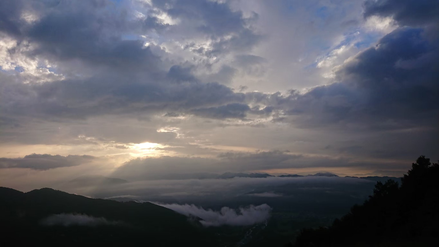 Langit mendung yang diterangi cahaya yang menembus pegunungan