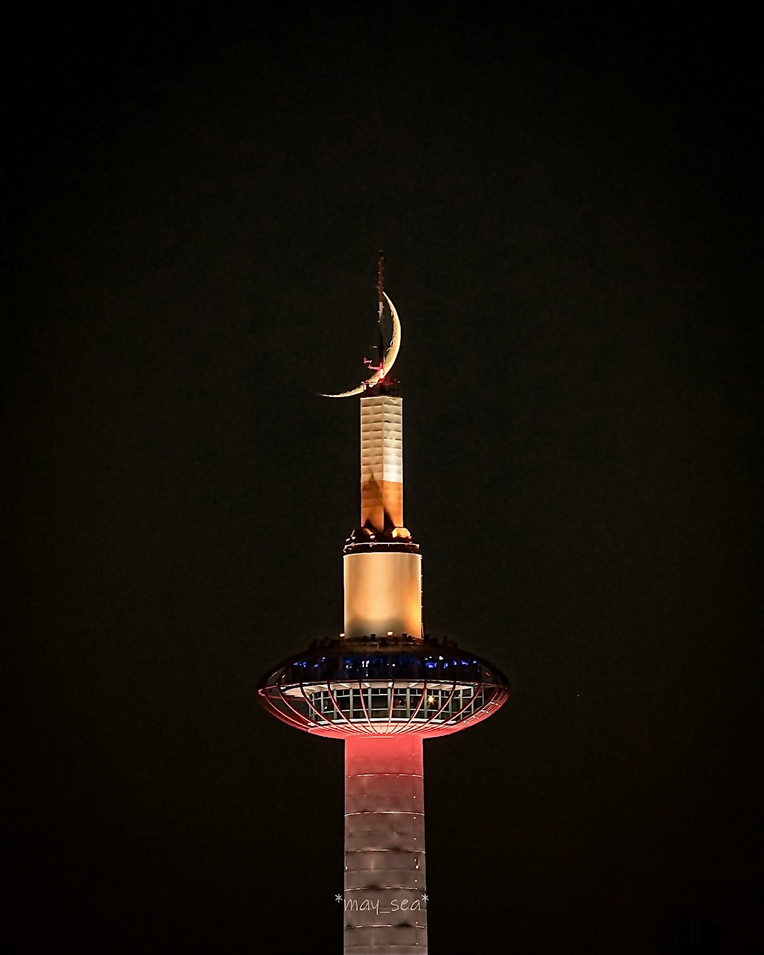 Golden crescent atop a mosque minaret illuminated against a black background