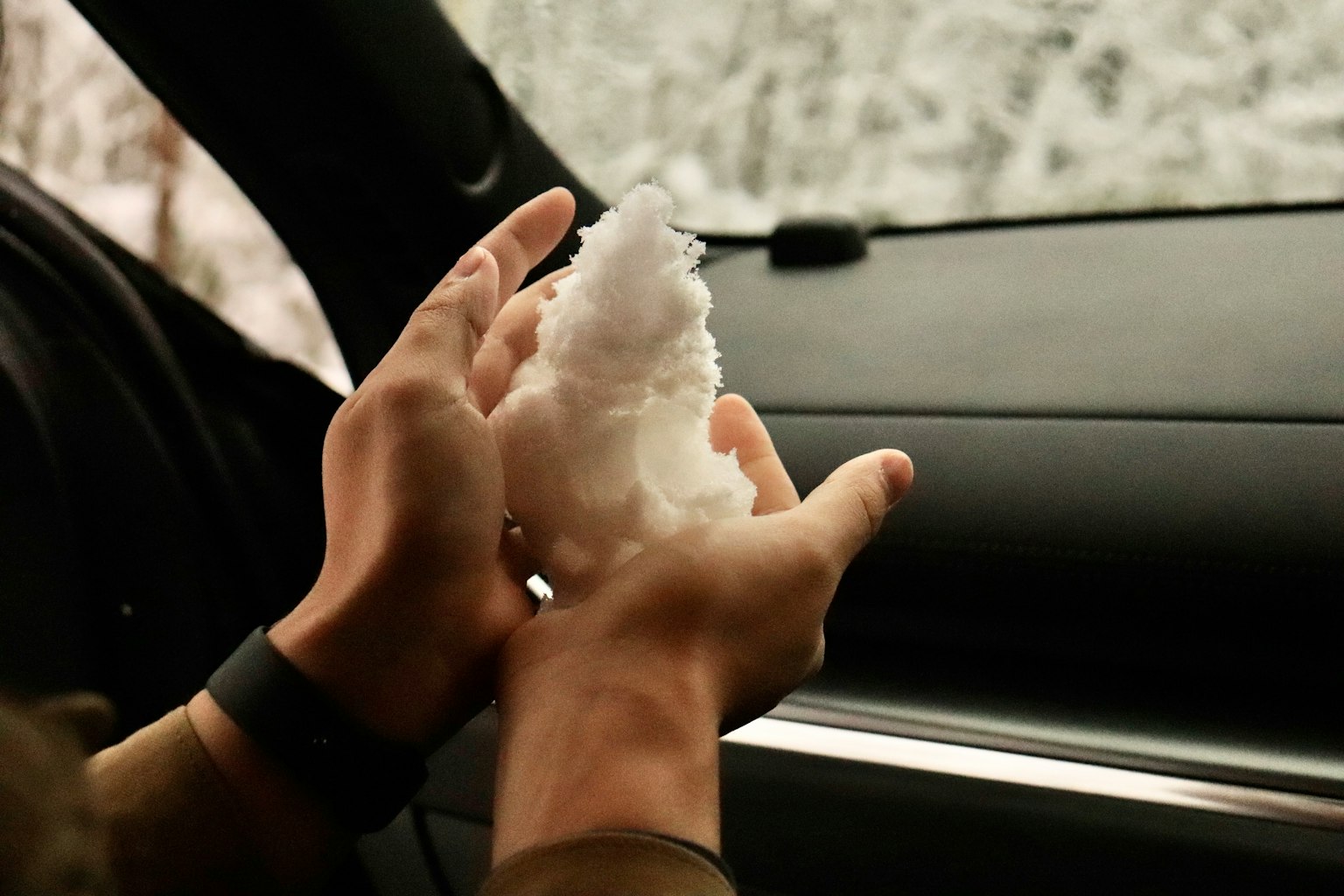 Primo piano di mani che tengono neve all'interno di un'auto