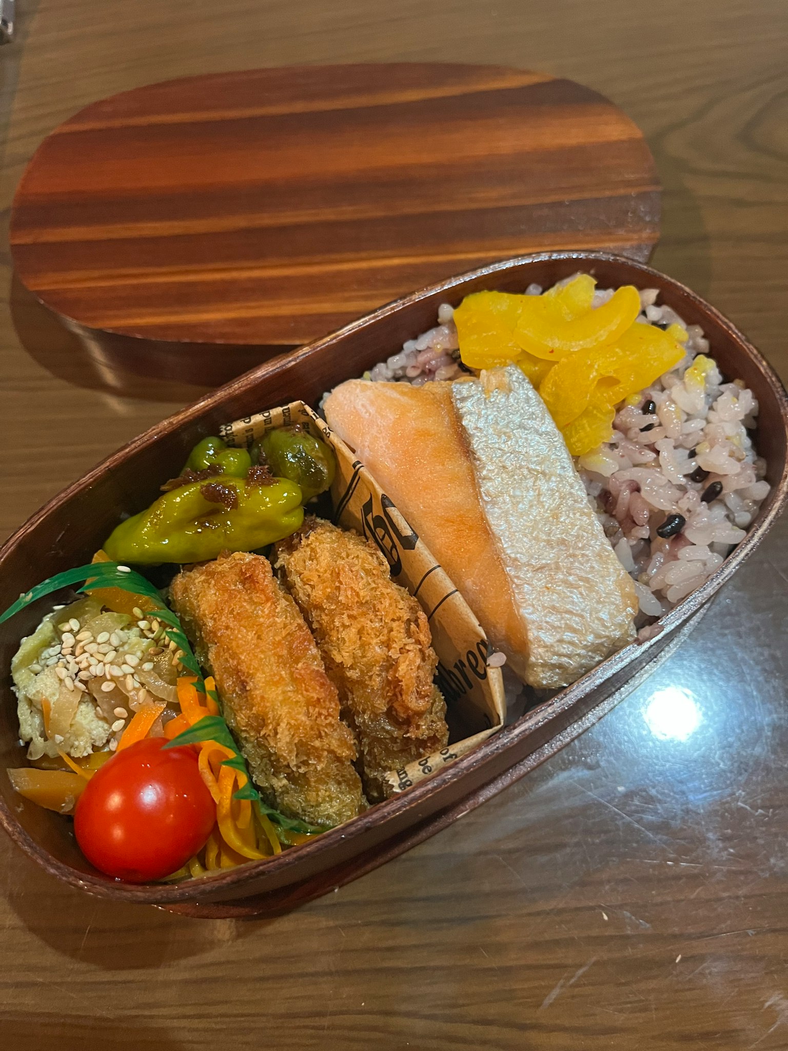 一个装满日本料理的木制便当盒，包含米饭、烤三文鱼、炸丸子、蔬菜和樱桃番茄
