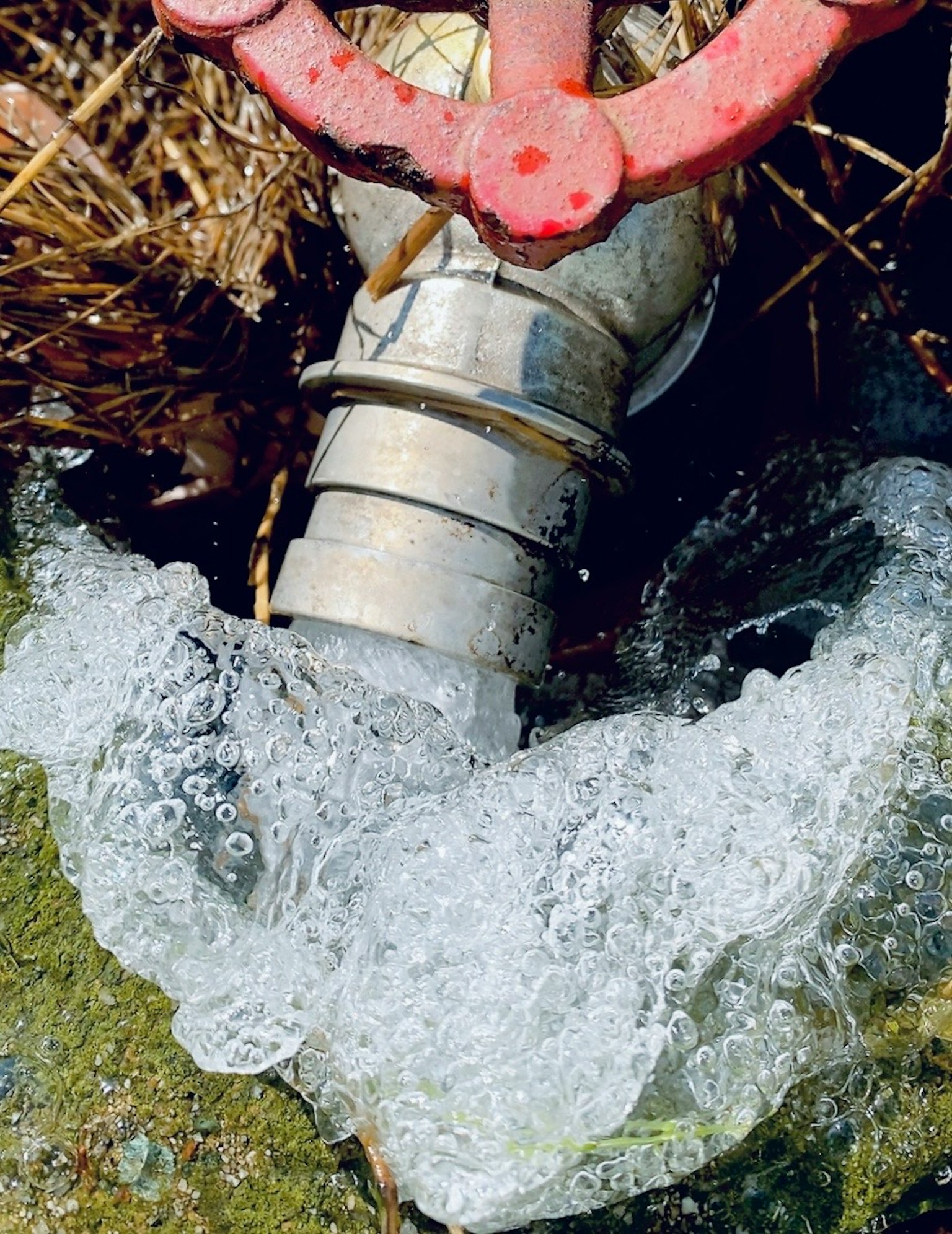 Metal pipe with a red valve releasing water and bubbles