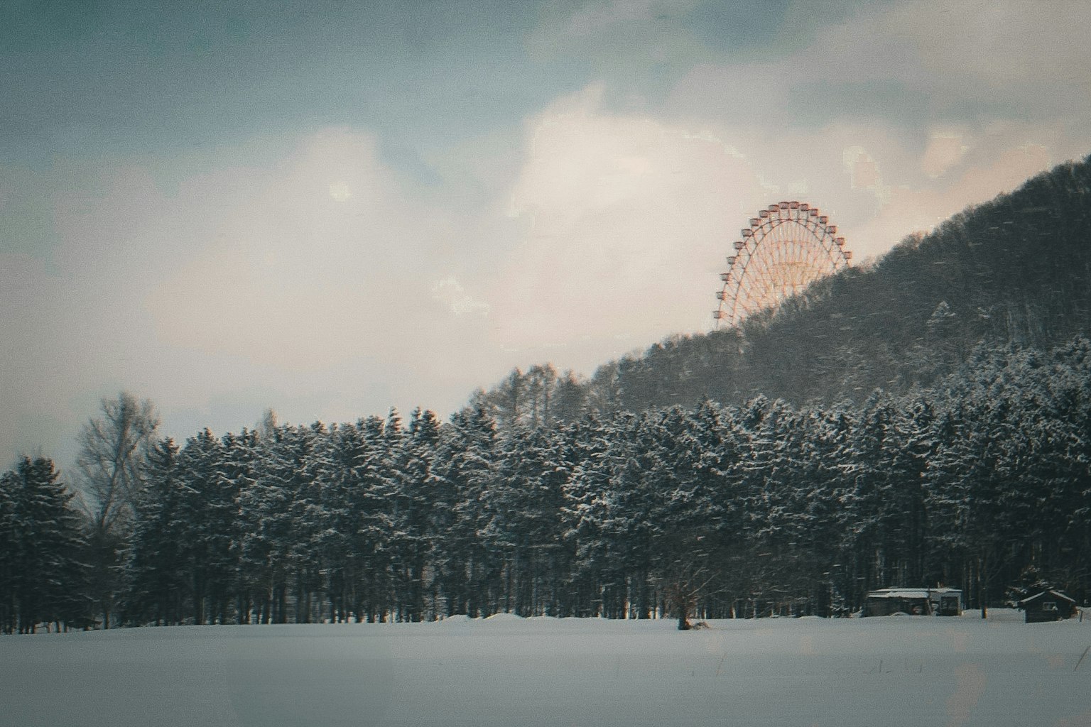 Riesenrad hinter einem verschneiten Wald und einem Berg sichtbar