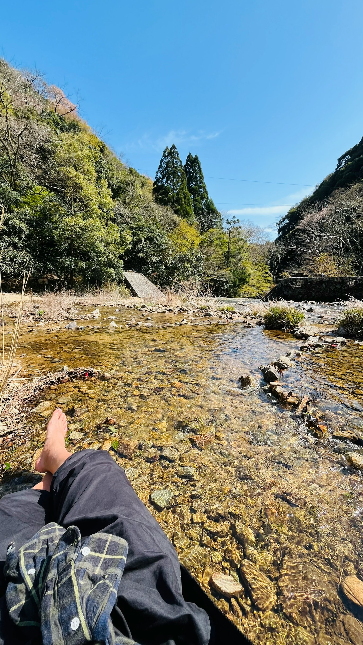 Una persona che si rilassa vicino a un fiume con acqua limpida e montagne sullo sfondo