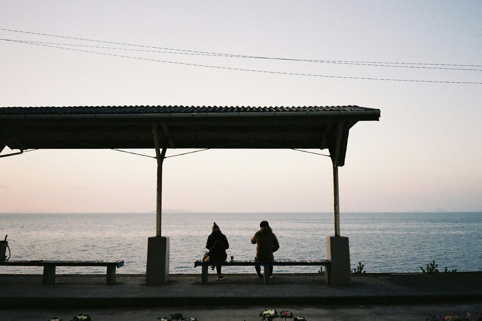 Silhouetten von zwei Personen, die unter einem Schutzdach am Meer sitzen, während die Sonne untergeht