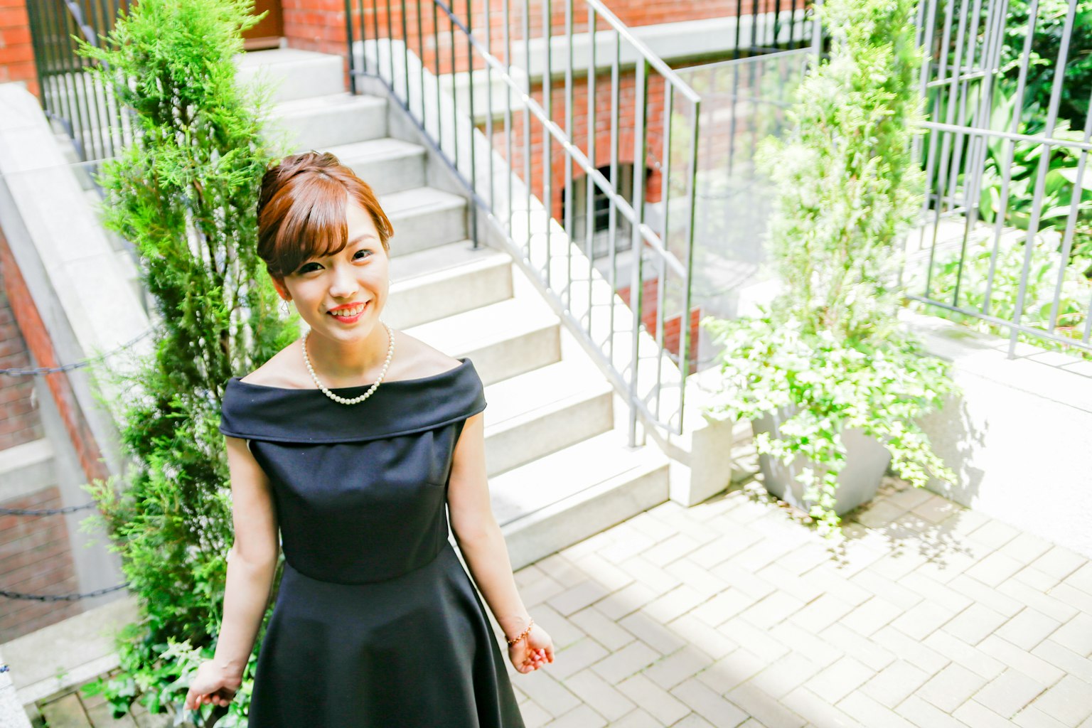 Una mujer con un vestido negro sonriendo frente a unas escaleras con vegetación