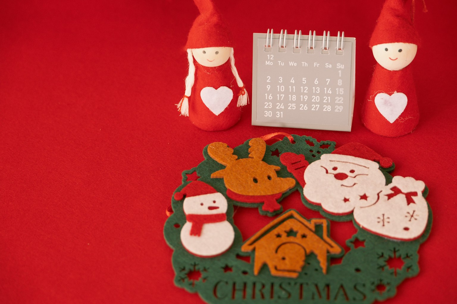Adegan dengan dekorasi Natal di latar belakang merah yang menampilkan dua boneka bertopi merah sebuah kalender dan karangan bunga Natal