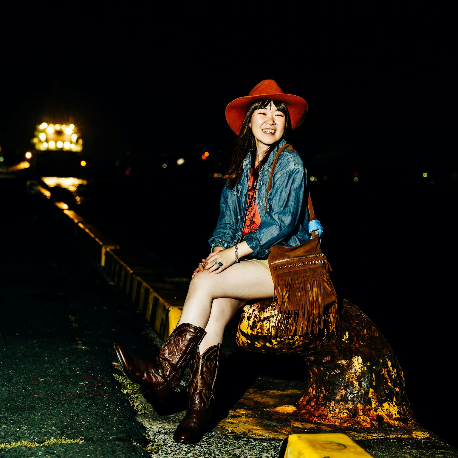 Une femme avec un chapeau rouge et des bottes de cowboy assise au port la nuit