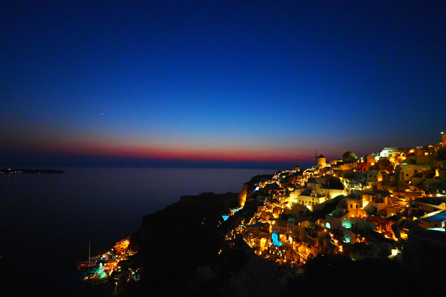 Vue nocturne d'une ville côtière avec des bâtiments illuminés et un ciel bleu profond