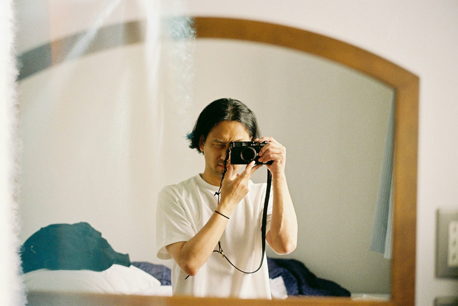 Autoritratto di un uomo con una macchina fotografica davanti a uno specchio che mostra parte di una stanza