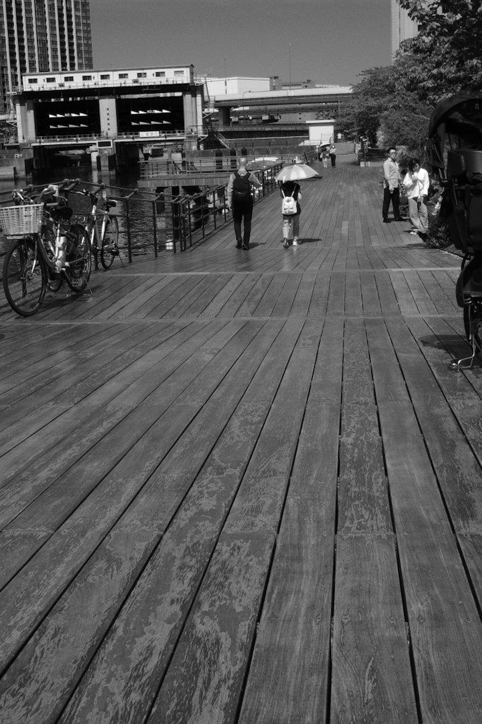 Schwarzweißbild eines Holzdecks mit Menschen, die gehen, und Fahrrädern